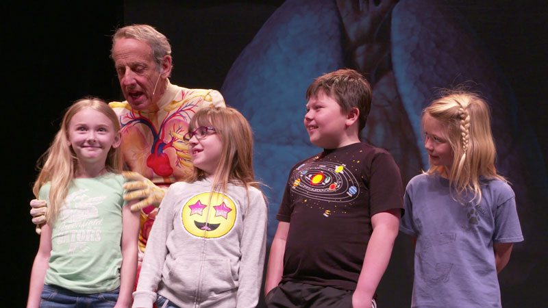 Slim Goodbody on stage with a group of children during a live Bodyology assembly.